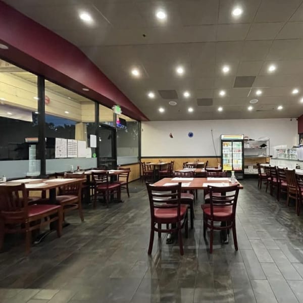 Interior of Akita Sushi Gourmet Inc. with empty tables, red chairs, and a sushi bar.