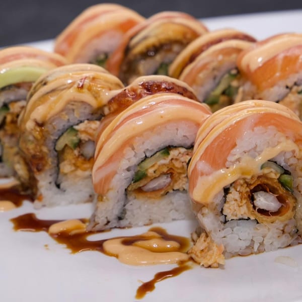 Close-up of Akita Sushi Gourmet's salmon and eel sushi rolls, drizzled with sauces on a white plate.