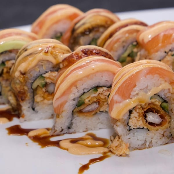 A close-up of Akita Sushi Gourmet's salmon and eel sushi rolls with creamy sauce and soy drizzle.