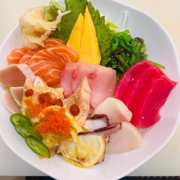 A colorful Akita Sushi sashimi bowl with various fish, roe, lemon, seaweed, and pickled ginger.