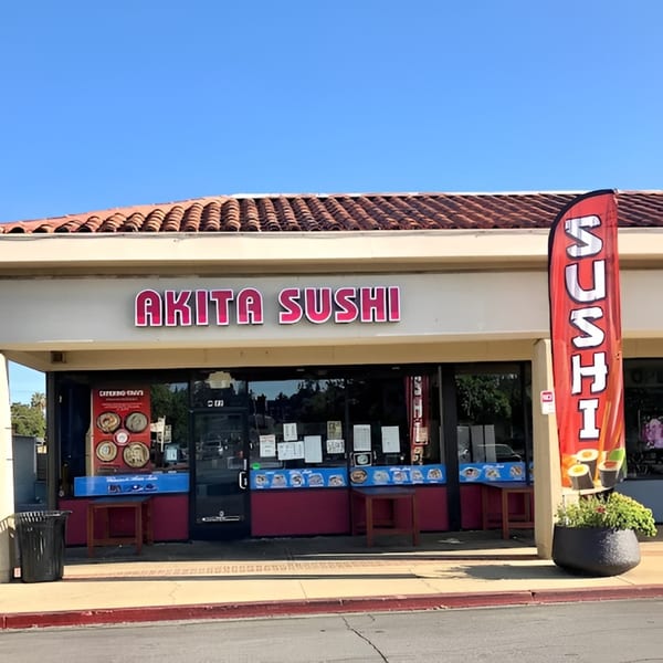 Exterior of Akita Sushi Gourmet Inc, featuring a red sushi flag and menu displays in the windows.