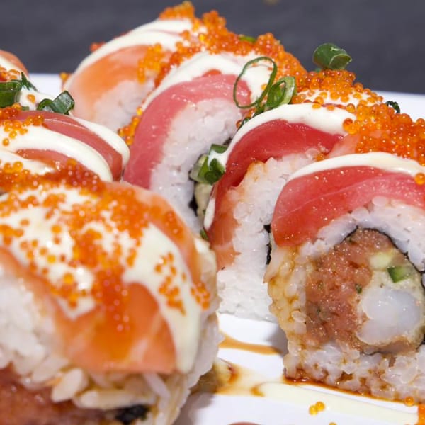 Close-up of Akita Sushi rolls topped with salmon, tuna, roe, mayonnaise, and green onions.
