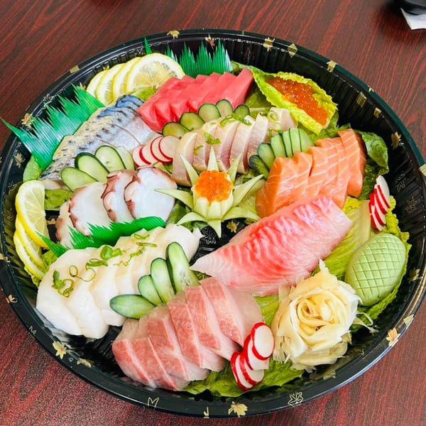 A large platter of Akita Sushi Gourmet's sashimi, including tuna, salmon, octopus, and scallops, garnished with lemon and cucumber.