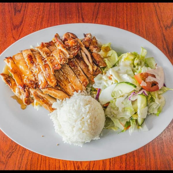 Teriyaki chicken with sesame seeds, a scoop of white rice, and a side salad on a white plate.