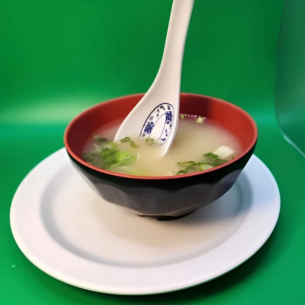 Miso soup with green onions and tofu in a black and red bowl with a white spoon.