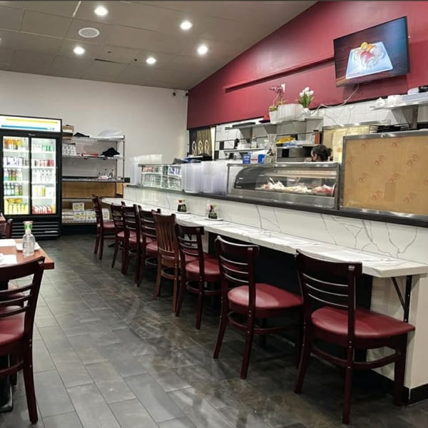 Interior of Akita Sushi Gourmet Inc. with a sushi bar, red chairs, and a TV displaying sushi.