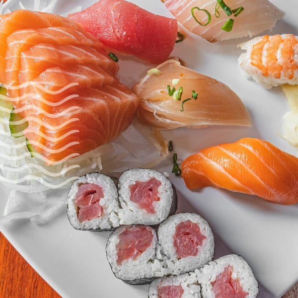 A white plate filled with various Akita Sushi Gourmet sushi and sashimi, including tuna and salmon.